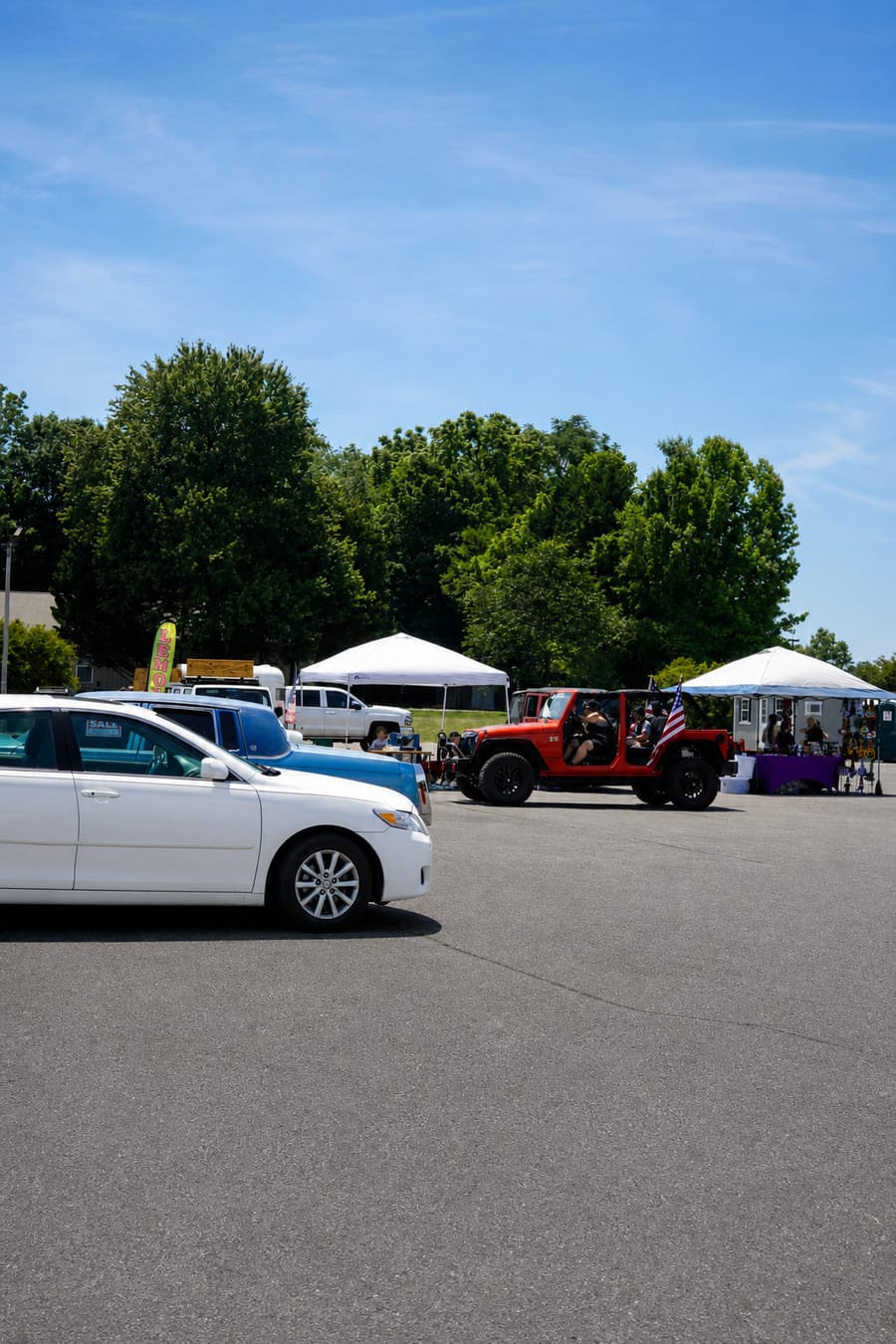 Wide shot of the lot with Jeeps, a black overland rig, and vendor tents at the Jeep Jam.