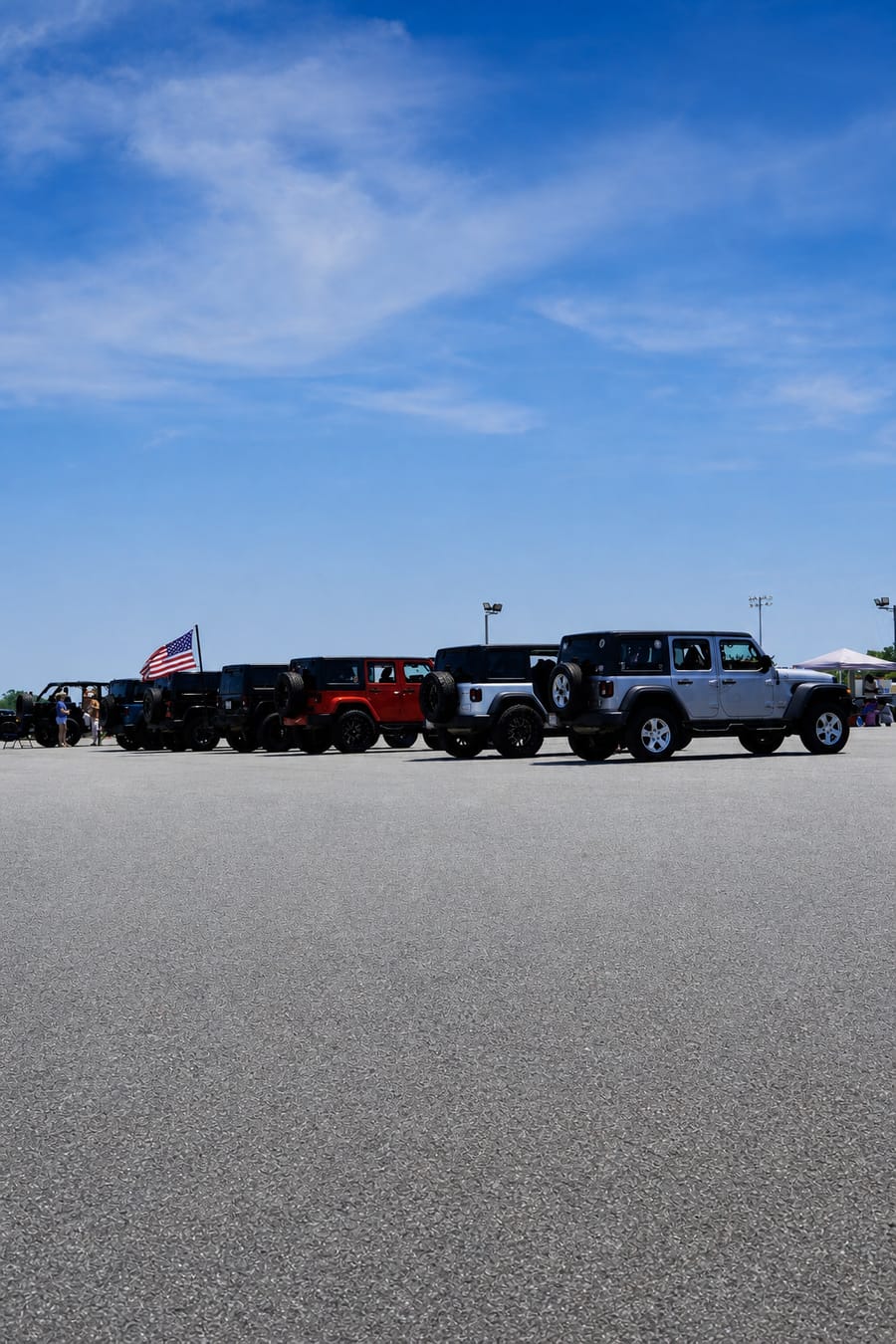 Long line of lifted Jeep Wranglers parked side by side at the Jeep Jam meet in Mocksville with an American flag flying.