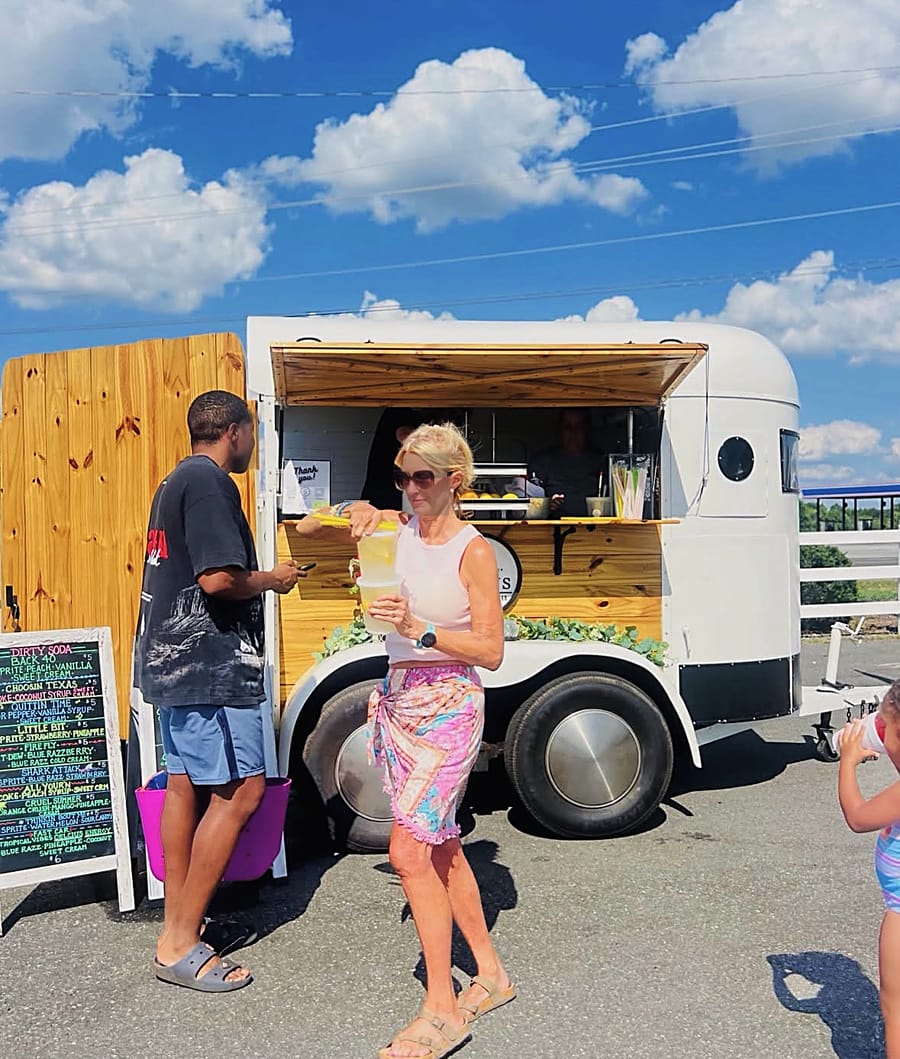 A lemonade and dirty-soda trailer serving cold drinks on the lot under a blue sky