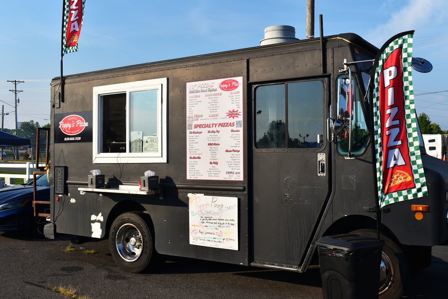 Black pizza food truck with its menu board and flag out on the lot at the truck meet.