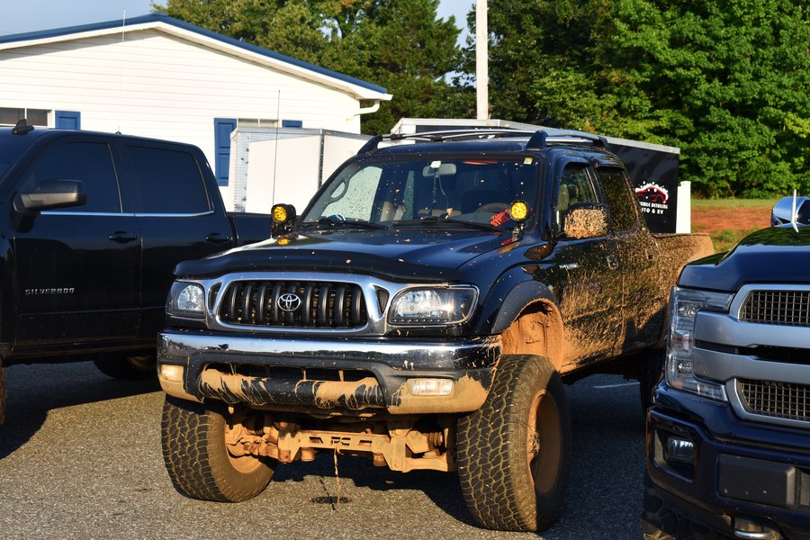Mud-covered lifted Toyota Tacoma parked between trucks at the meet on Highway 601.