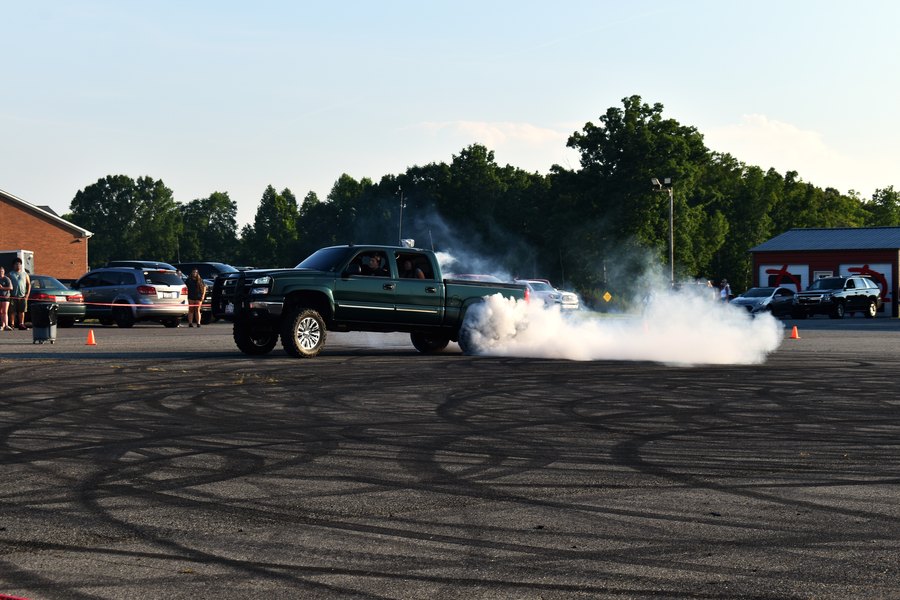 Dark green lifted truck kicking up tire smoke across the lot at the truck meet.