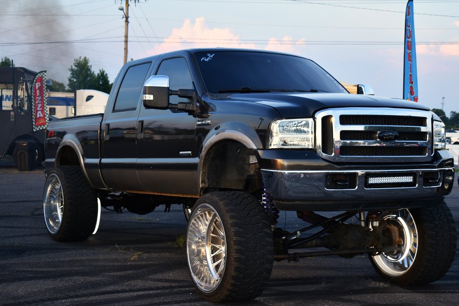 Black lifted Ford on chrome wheels parked beside the food truck row at the truck meet.