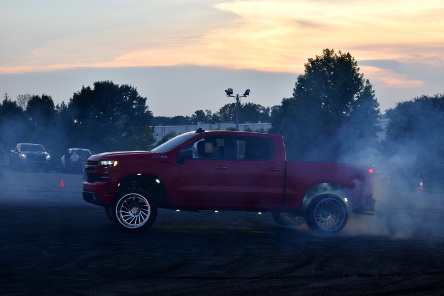 Maroon lifted truck laying down a burnout in a cloud of smoke at dusk during the truck meet in Mocksville.