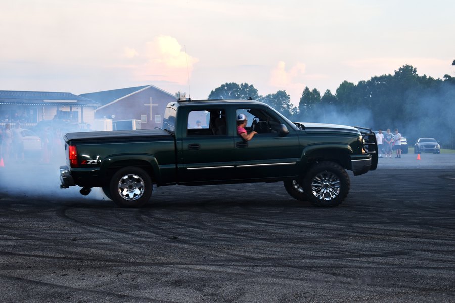 Dark green truck rolling through tire smoke at sunset during the Mocksville truck meet.